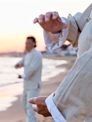 Two older people practicing Taijiquan on the beach at sunset, close up on hands